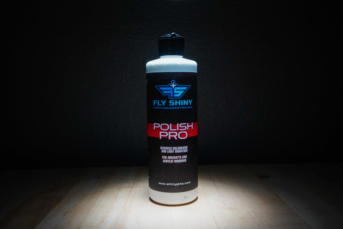 A bottle of Fly Shiny Polish Pro stands in front of a gleaming aircraft, showcasing a flawless high-gloss finish on its paint and superior clarity in its windows.